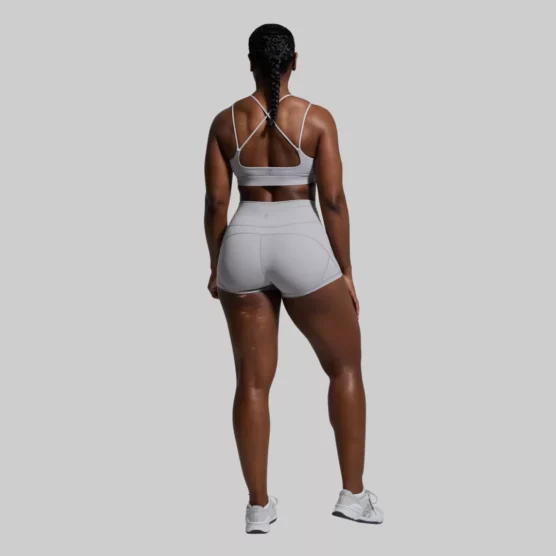 En kvinne som står med ryggen mot kameraet. Hun har på seg Exhale lysegrå sports-bh og New Heights shorts i samme farge. Sports-bh'en har to stropper på hver side. To av stroppene krysser hverandre bak på ryggen.