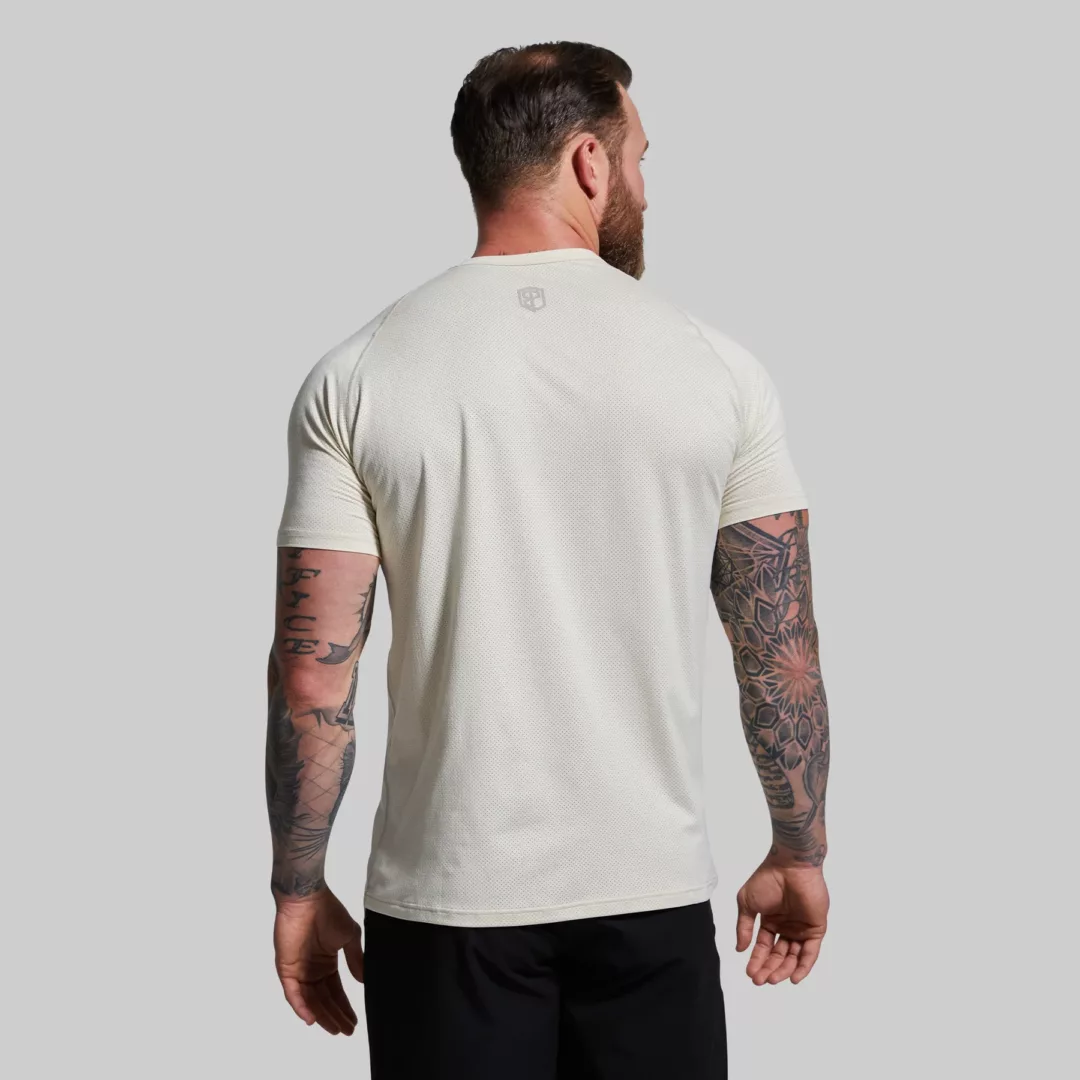Mann som står med ryggen mot kameraet med en kremhvit teknisk Heritage treningstrøye. T-skjorten har lett og luftig stoff, og den har en liten Born Primitive logo øverst på ryggen.