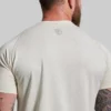 Mann som står med ryggen mot kameraet med en kremhvit teknisk Heritage treningstrøye. T-skjorten har lett og luftig stoff, og den har en liten Born Primitive logo øverst på ryggen.