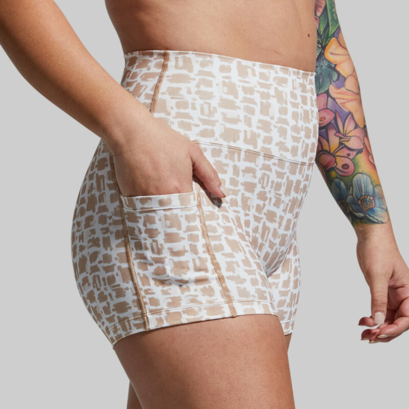 Kvinne med hvit og lysebrun mønstrete trenings-shorts med lomme på én side.