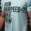 Lift List T-Shirt. Mann iført turkis t-skjorte med sort skrift foran. Teksten sier "Run, Burpees, Bike, Row, Lift", der alt er gjennomstreket utenom "Lift".