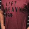 Mann iført mørkerød t-skjorte med sort tekst foran. Teksten sier "Lift Heavy Ish".