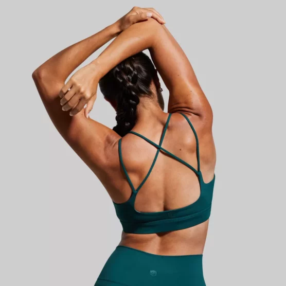 Kvinne med mørkegrønn sports-BH. Sports-BHen har kryssende stropper på ryggen.