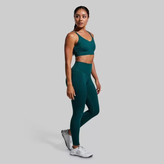 Kvinne med mørkegrønn sports-BH. Sports-BHen har kryssende stropper på ryggen.