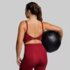 Kvinne med mørkerød sports-BH. Sports-BHen går et stykke ned på magen og har tvinnede stropper bak.