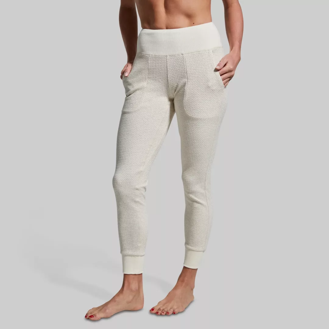 Kvinne iført en dus hvit joggebukse. Buksen har lommer og strikk nederst på beina. Buksen er høy i livet.