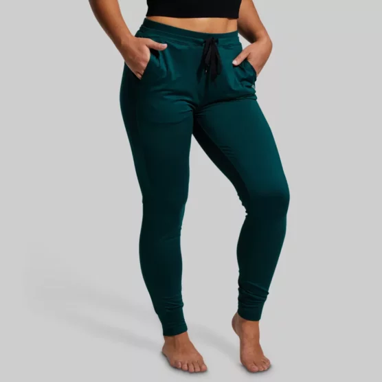 Kvinne med mørkegrønn joggebukse med lommer foran og bak. Buksen har knyting i livet.