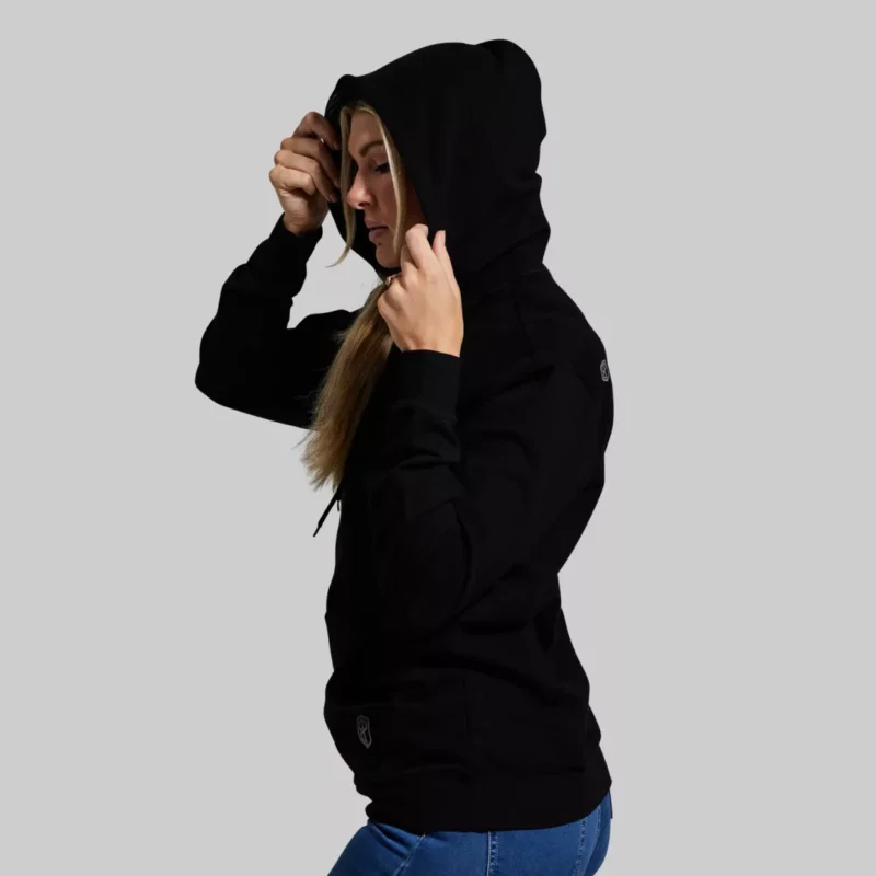 Kvinne står med siden mot kamera iført en sort hettegenser.