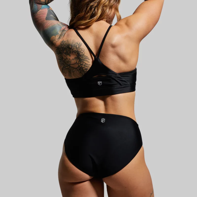 dame iført sort bikini top, overdel med to tråder som krysser i ryggen og sort bikinitruse, bikini bottom. sett bakfra